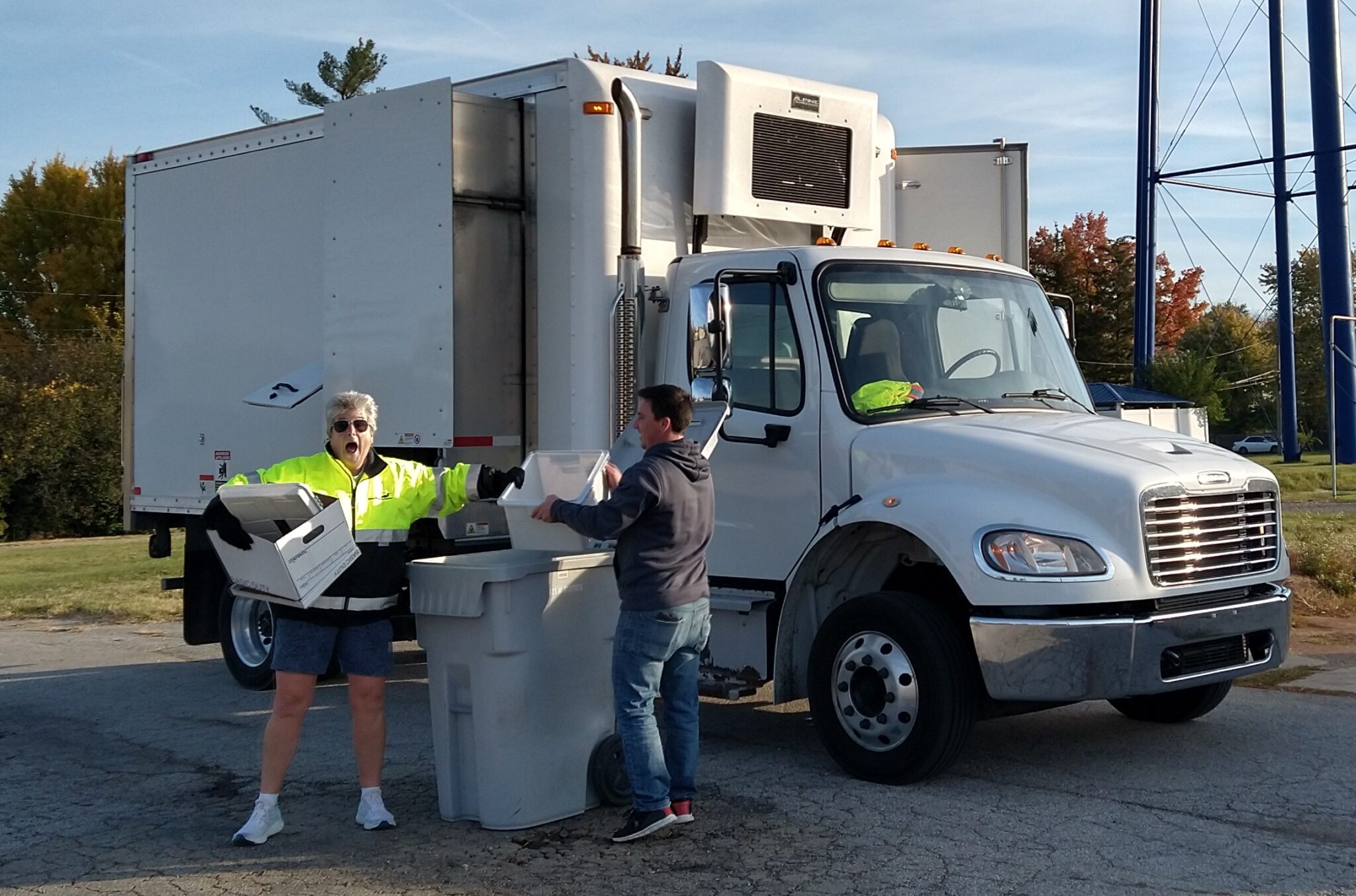 Woman and man placing paper for shredding into a large receptacle in front of a shredding truck
